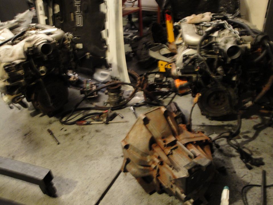 Two disassembled engines and a transmission are on a garage floor