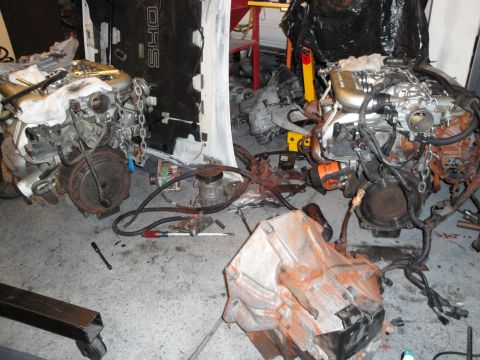 1989 Ford Taurus - Two engines and transmissions are laid out on the floor of a garage, appearing to be undergoing repair or disassembly.