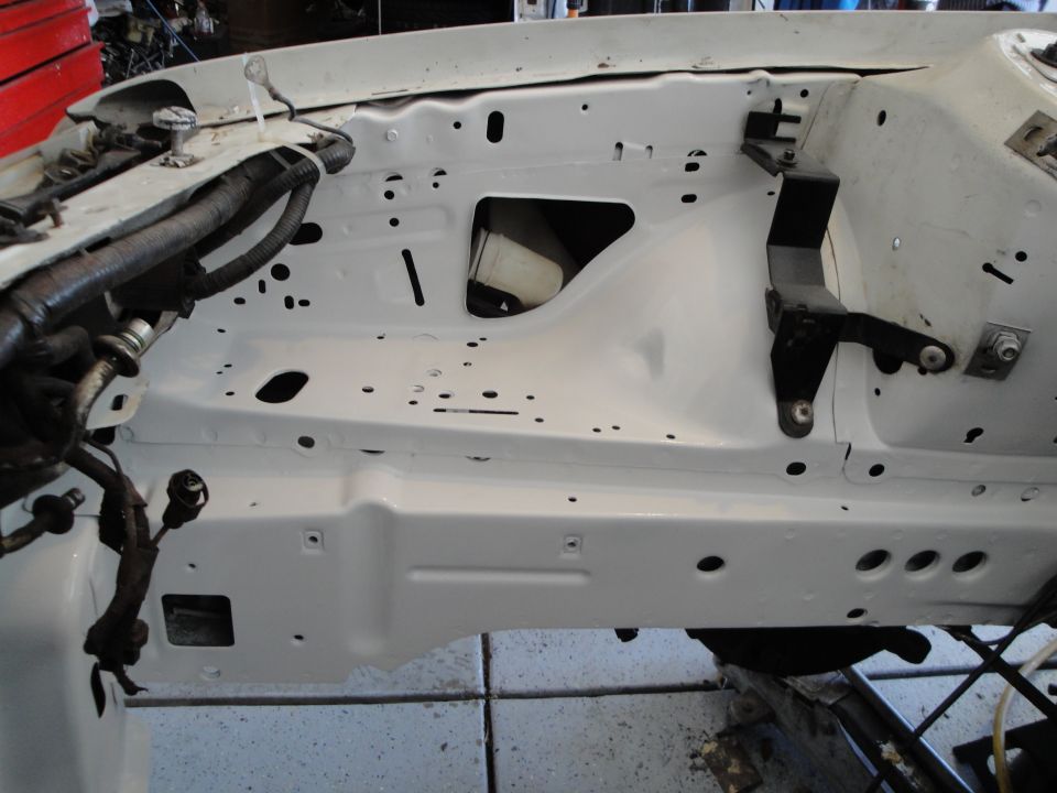 White painted engine bay with wiring harnesses and brackets. Some holes and cutouts are visible