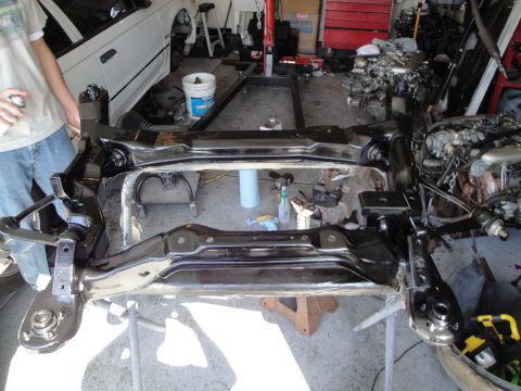 1989 Ford Taurus - A car's subframe assembly is being worked on in a garage, with an engine visible in the background.