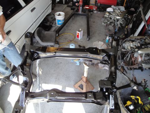 1989 Ford Taurus - A car frame is shown in a garage setting, with an engine hoist and additional engines visible in the background.