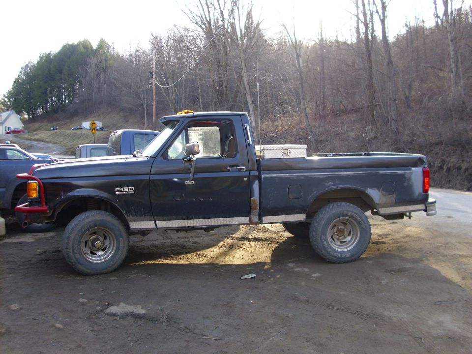 Side view of a black 1995 Ford F-150 pickup truck with a red front bumper and a toolbox in the bed