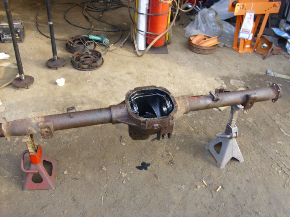 Rusty rear axle assembly on jack stands, with driveshafts and brake drums nearby