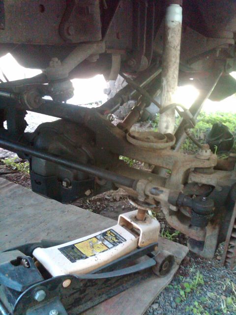1978 Ford Bronco - Close-up view of vehicle front suspension components, including the axle and steering linkage, held by a floor jack.