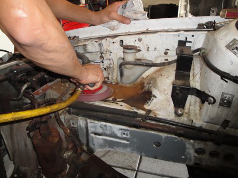 1989 Ford Taurus - A person sands the engine bay of a vehicle, revealing rust and dirt beneath the surface.