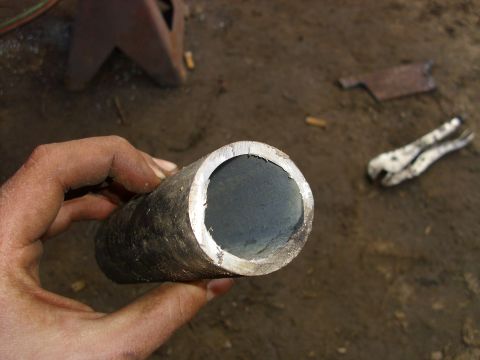 1995 Ford F-150 - A metal pipe is held in a hand, with a pair of pliers and other tools visible in the background.