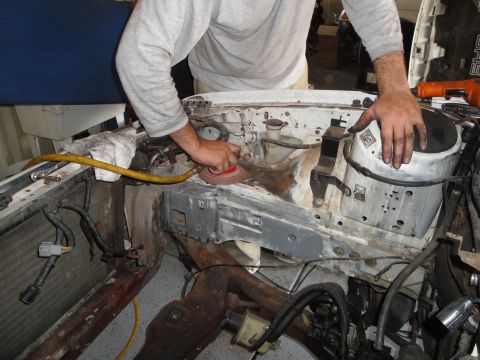 1989 Ford Taurus - A person sands the engine bay of a vehicle, preparing it for an engine swap or repair.