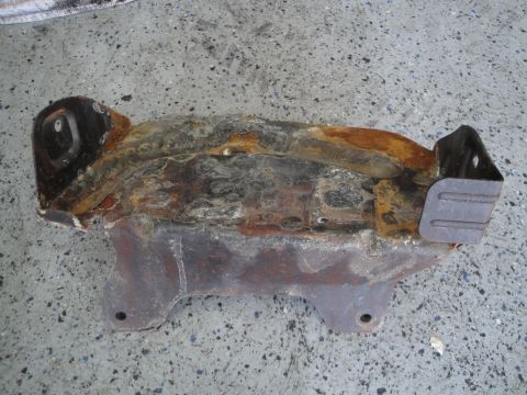 1989 Ford Taurus - This heavily corroded engine component shows significant wear and tear, resting on a textured concrete surface.