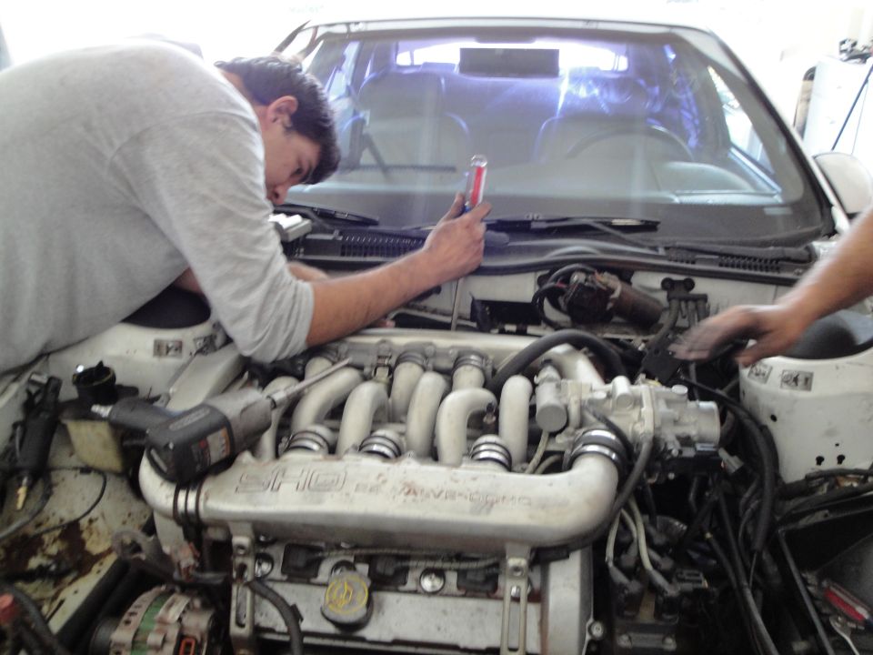 Engine bay with two people working on it, one holding a red tool