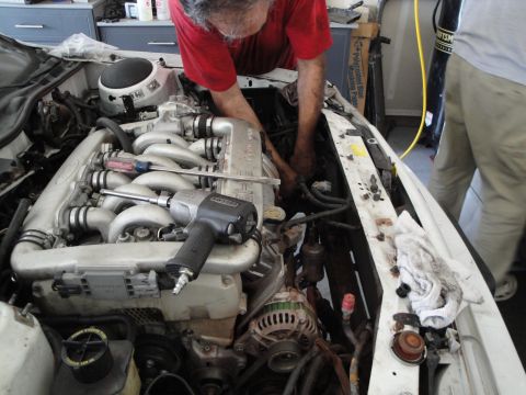 1989 Ford Taurus - Two people are working on the engine of a car, with various tools and engine parts visible in the bay.