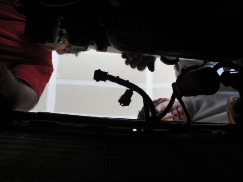 1989 Ford Taurus - Two individuals are seen working on the engine of a vehicle from an unusual low-angle perspective.