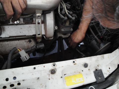 1989 Ford Taurus - Mechanic's hands are busy working on the engine of a vehicle, with various wires and components in view.
