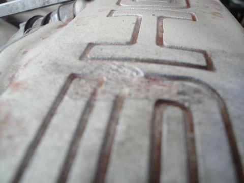 1989 Ford Taurus - A close-up view of a textured engine valve cover shows raised lettering and some reddish staining.