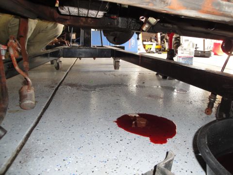1989 Ford Taurus - The underside of a vehicle is visible, supported by a lift, with a spill of red fluid on the floor.