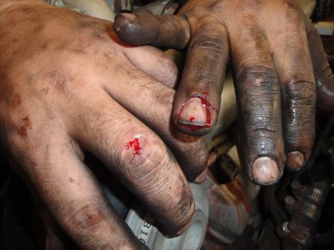 1989 Ford Taurus - Mechanic's hands show bloody cuts and grime, likely from working on an engine.