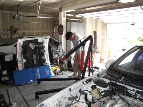 1989 Ford Taurus - Mechanic working on a car's engine bay in a garage, with another vehicle's hood nearby.