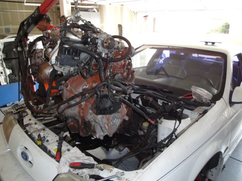 1989 Ford Taurus - A mechanic uses an engine hoist to remove the engine from a white car in a garage.