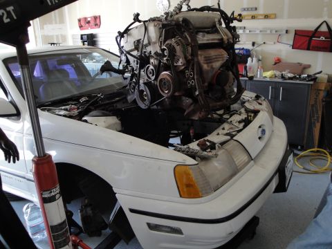 1989 Ford Taurus - A 1989 Ford Taurus is in a garage with its engine being removed by a hoist.