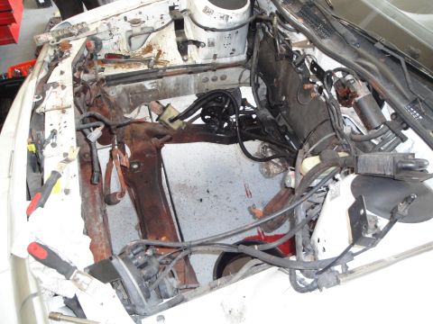1989 Ford Taurus - The engine bay is largely empty, showing rusted structural components and wiring, suggesting an engine swap or removal.