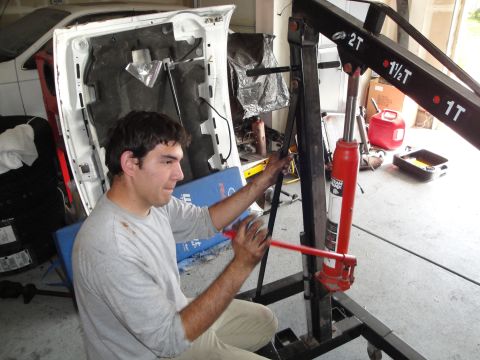 1989 Ford Taurus - Man works on an engine hoist in a garage, with a car's hood open nearby.