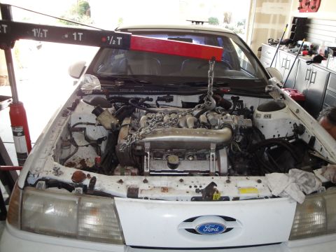 1989 Ford Taurus - Engine hoist lifting the engine out of a white 1989 Ford Taurus.