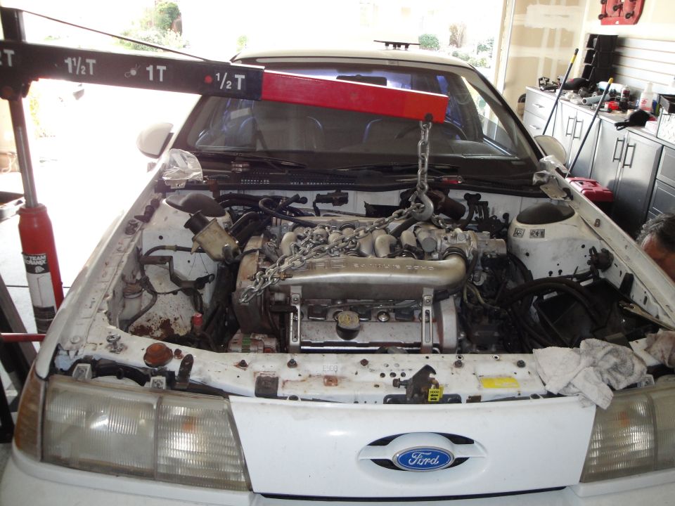 White 1989 Ford Taurus engine bay with engine being removed by an engine hoist