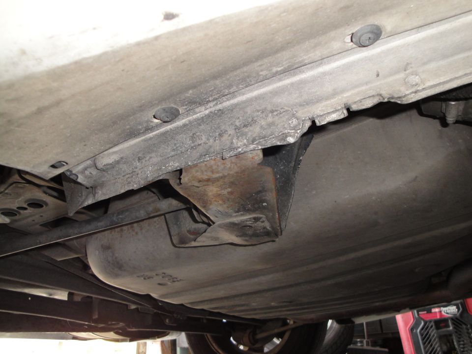 Undercarriage of a vehicle showing a fuel tank and rusted structural components