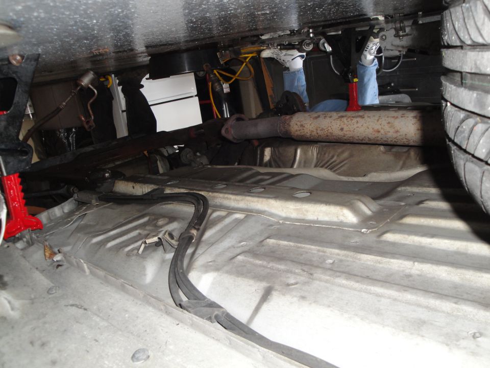 Underside of vehicle showing exhaust pipe, fuel lines, and tire