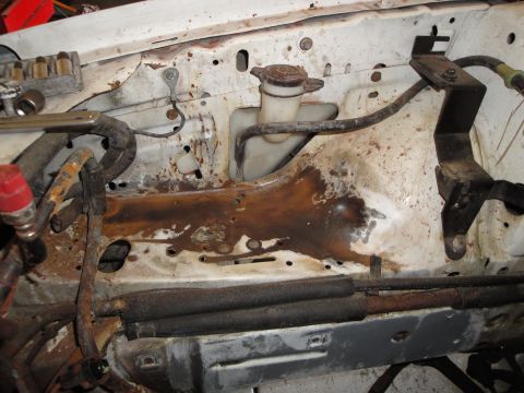 1989 Ford Taurus - The engine bay shows significant rust and wear on its components and surrounding metal structure.