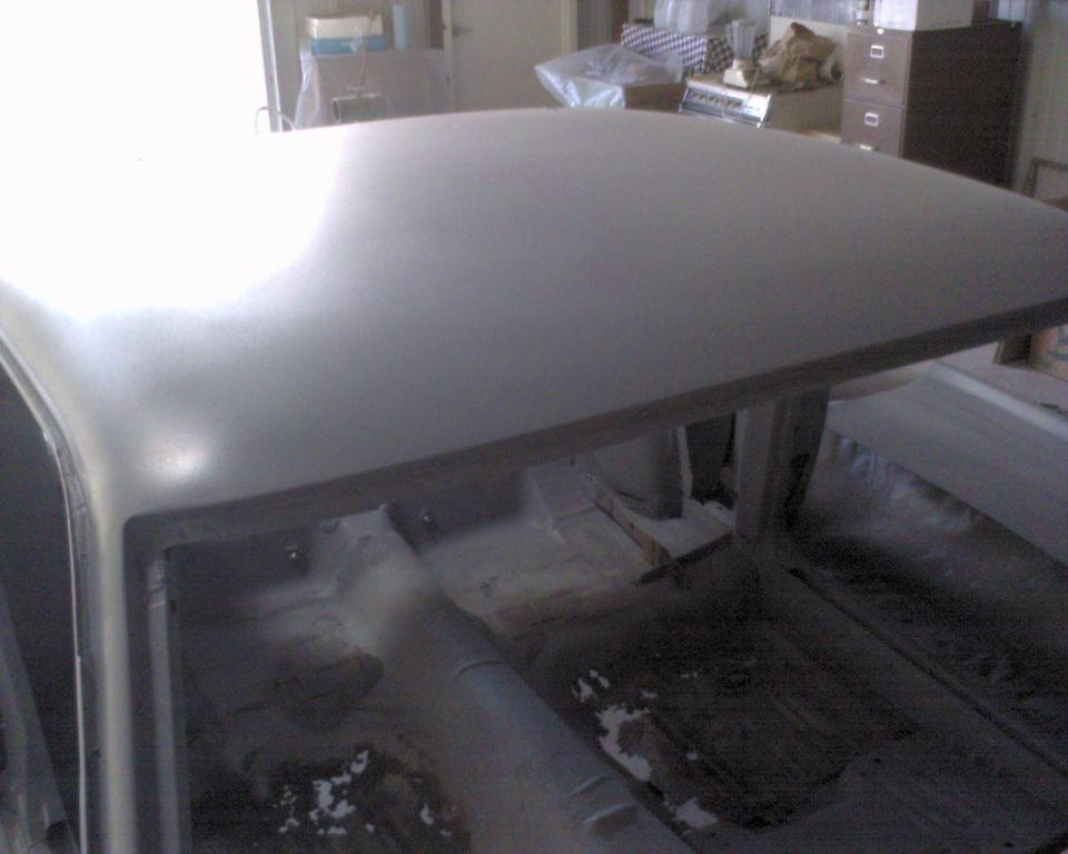 Gray primered roof of a stripped Mustang body shell with bare interior floor pan visible, inside a shop