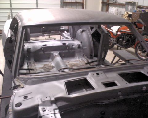 1970 Ford Mustang - Stripped 1970 Ford Mustang body undergoing restoration work, with a motorcycle in the background.
