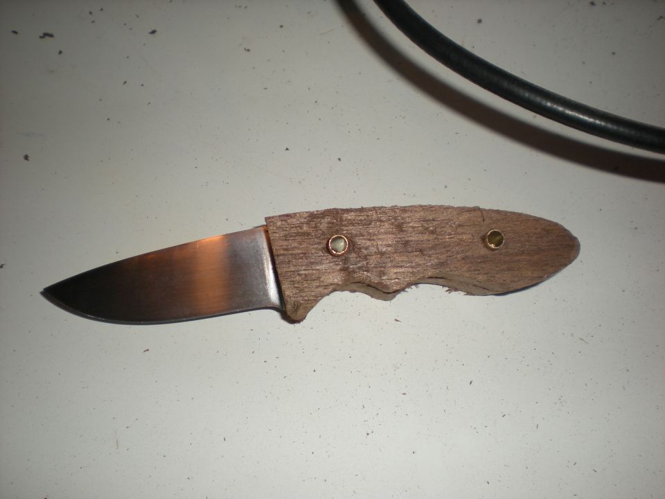 Knife with a metal blade and a rough wooden handle held together with brass pins. A black cable is visible in the background