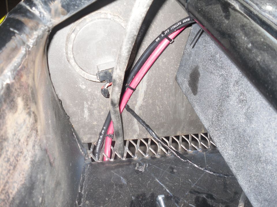 Battery cables and wiring routed through a metal grate, with a circular housing visible