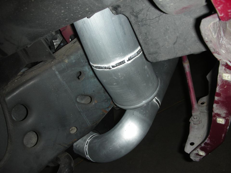 Close-up of custom aluminum exhaust pipes with visible welds, attached to a vehicle's undercarriage