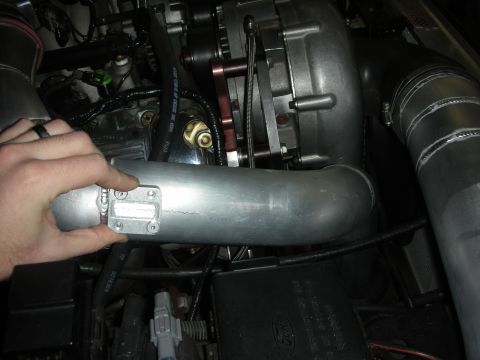 1992 Ford Crown Victoria - Close-up of a supercharger and intake piping in an engine bay, with a sensor being held.