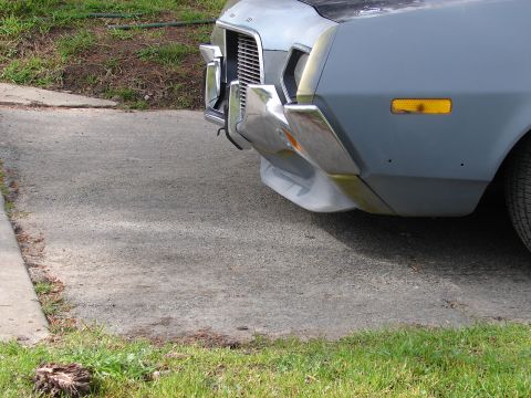 1973 Ford Ranchero - The front end of a primer gray 1972 Ford Ranchero is visible, showing its chrome bumper and grille.