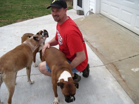 1992 Ford Mustang - A man kneels on a driveway interacting with three boxer dogs. Text is visible on his shirt and hat.