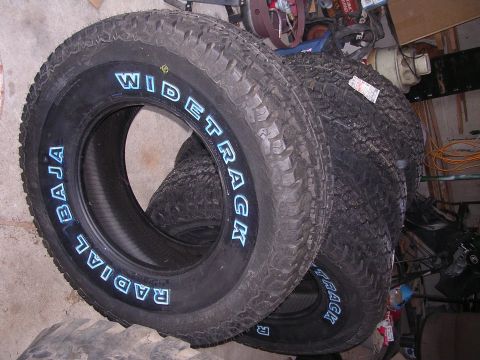 1979 Ford F-150 - A stack of off-road tires, including one with prominent white lettering, are shown in a garage setting.