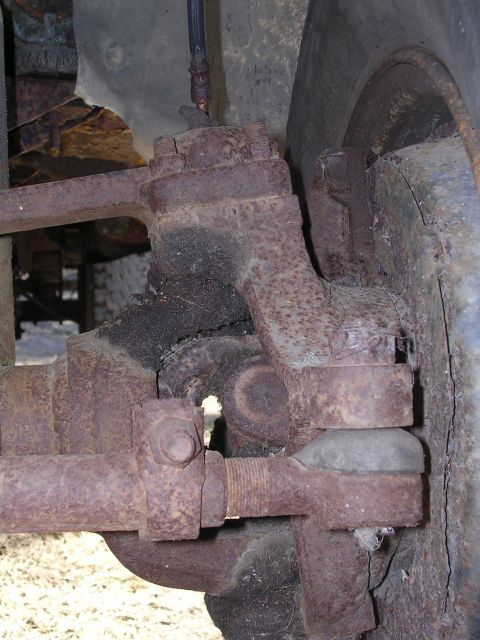 1979 Ford F-150 - This image shows a heavily rusted steering linkage assembly and a portion of a tire on a vehicle.