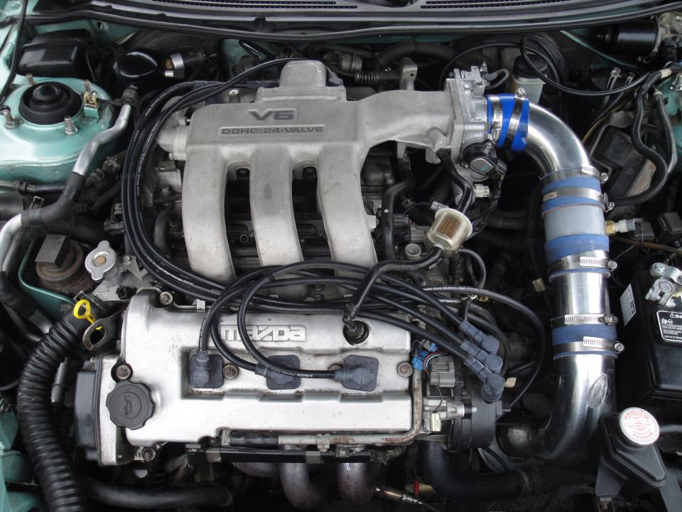 Engine bay with Mazda V6 DOHC 24-valve engine and polished aftermarket intake pipe in a green car
