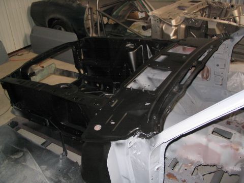1970 Ford Mustang - The body shell of a 1970 Ford Mustang is shown from the front, in a workshop setting with other vehicle parts visible.