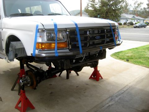 1996 Ford Bronco - The front of a Ford truck is elevated on jack stands, with blue tape securing the hood and grille area.