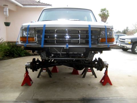 1996 Ford Bronco - Front view of a white Ford truck with its suspension disassembled and supported by jack stands.