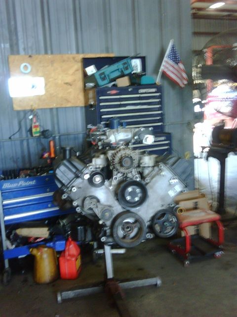 2005 Ford Crown Victoria - An engine is mounted on a stand in a workshop, surrounded by tools and equipment.