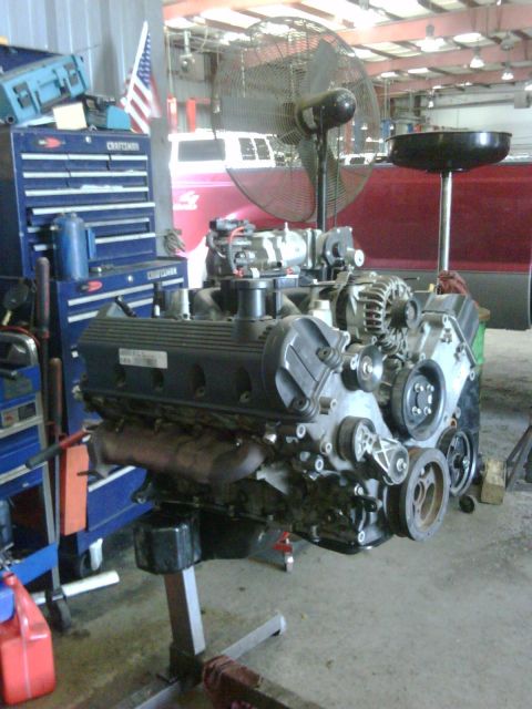 2005 Ford Crown Victoria - Engine assembly displayed on a stand, with a large industrial fan and tool chests visible in the workshop setting.