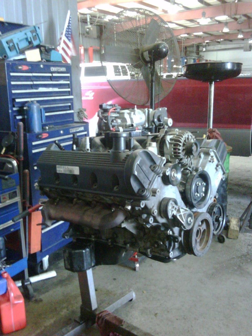 Engine on a stand in a garage, with tools and a fan in the background