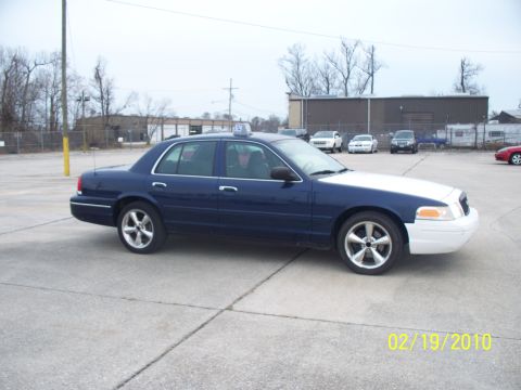 2005 Ford Crown Victoria - A blue and white 2005 Ford Crown Victoria taxi is parked outdoors on a cloudy day.