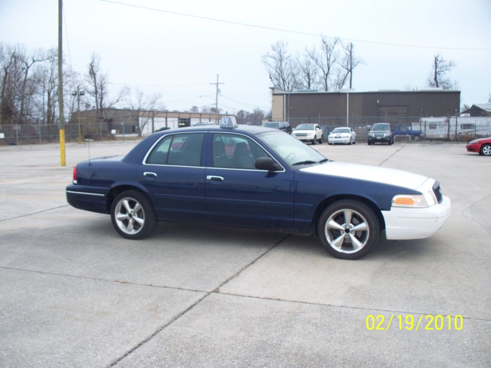 Blue and white 2005 Ford Crown Victoria taxi with a roof light, parked on concrete