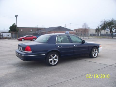 2005 Ford Crown Victoria - A dark blue 2005 Ford Crown Victoria sedan, identified as taxi number "$29", is parked in an open lot.