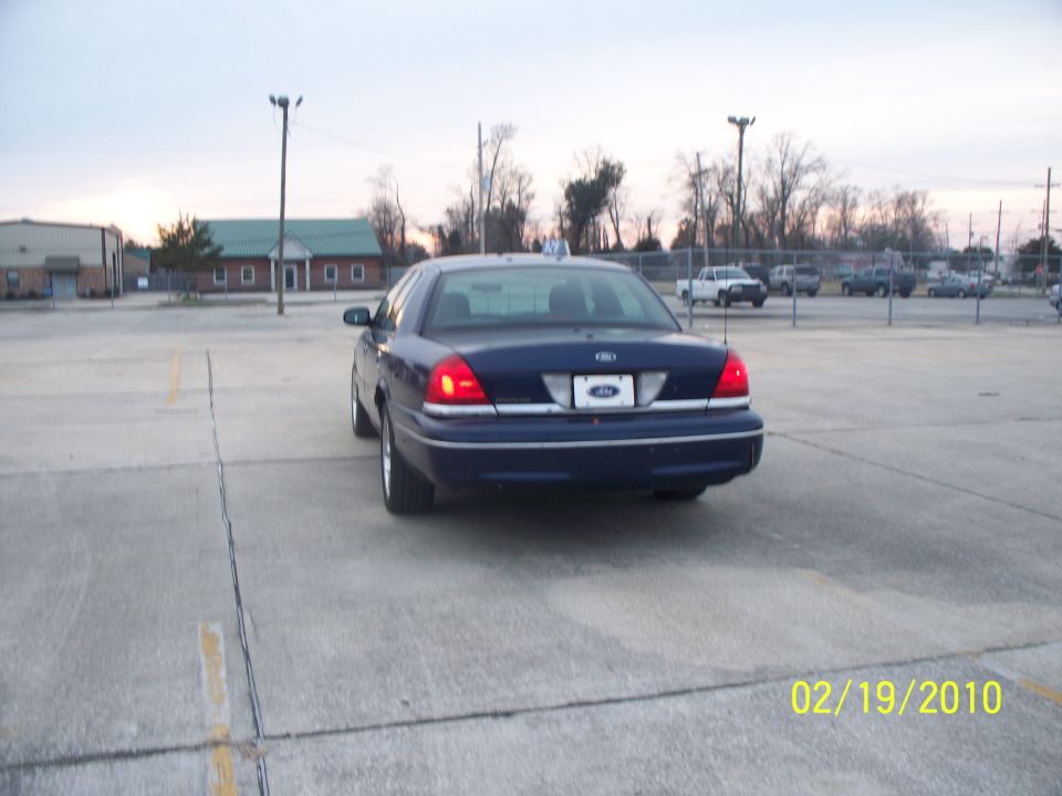 Dark blue Ford Crown Victoria parked in a lot. Rear view shows taillights and license plate